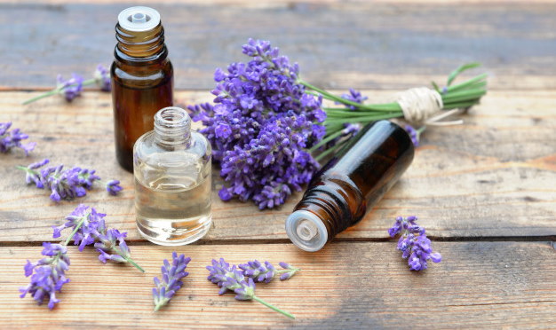 Image of three small essential oil bottles on what in table with a bouquet of purple lavender laying next to them