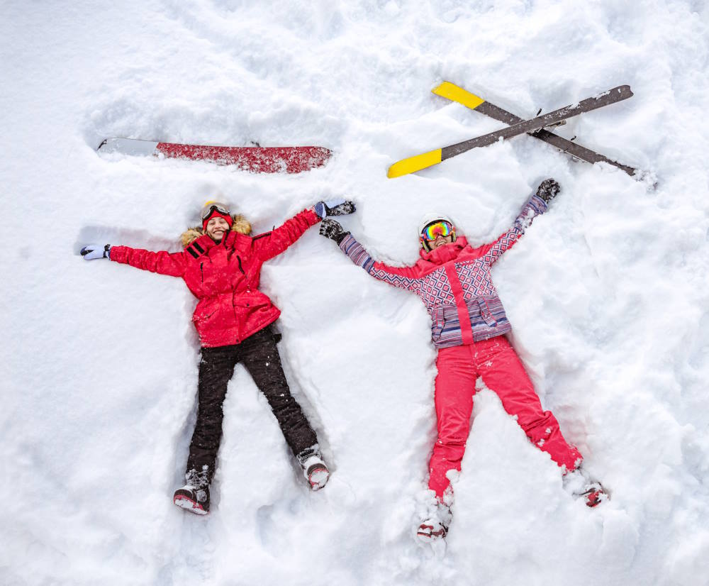 Image of 2 people taking a break from skiing and laying down in the snow making snow angels