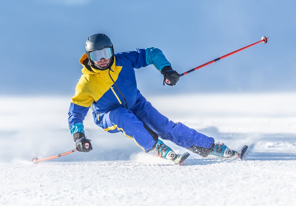 Man in a blue and yellow ski jacket skiing down a slope on a local NJ ski resort.