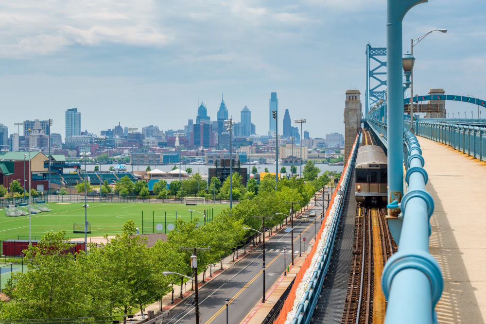 Image of a train on the skyline of Philadelphia, Pennsylvania, as seen from Camden New Jersey, featuring the Delaware River and Benjamin Franklin Bridge.