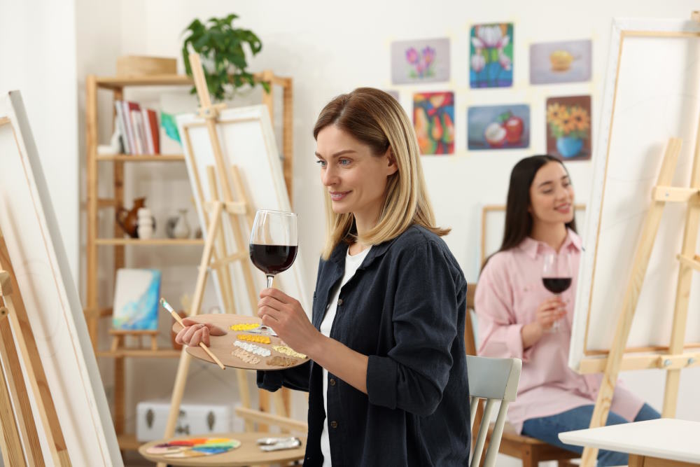 Image of two girls drinking wine while painting at a paint and sip class