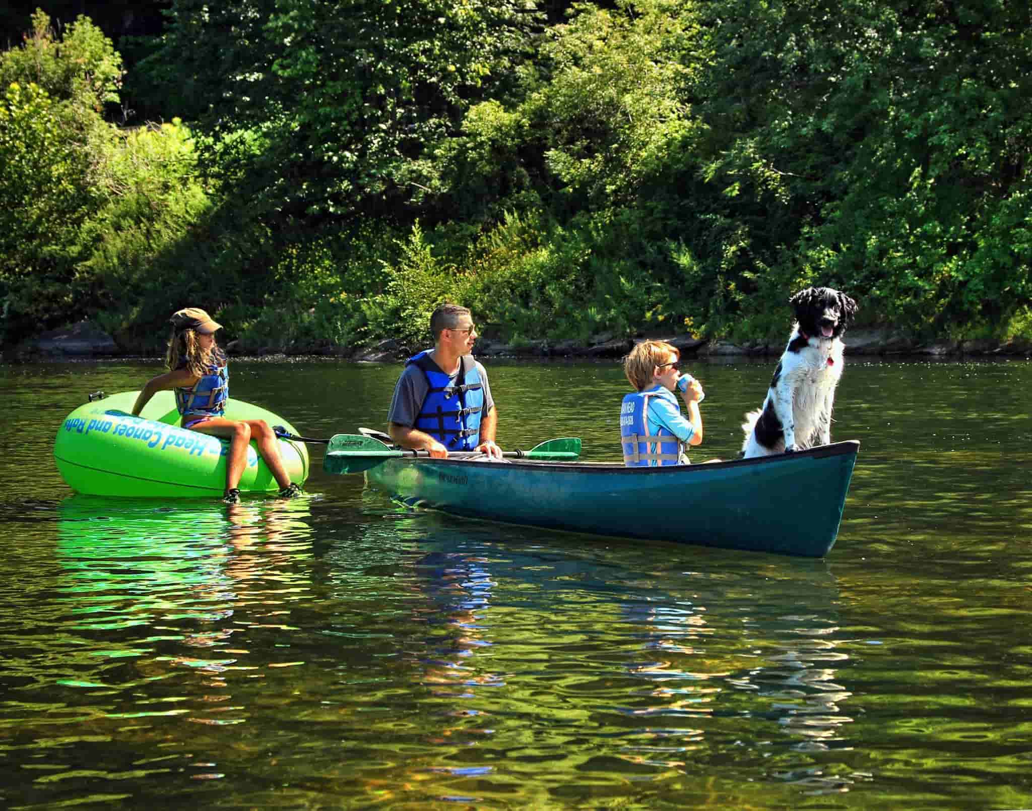 Image of a girl on a raft next to a canoe with a man a boy and a dog in it in Barryville NY