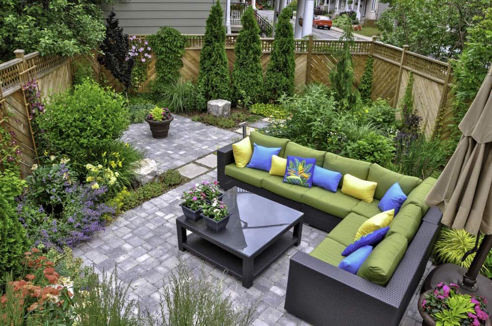 Image of a nicely landscaped backyard in NJ with a paver patio, a couch and arborvitaes.