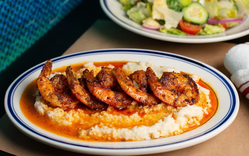 Photo of a plate with delicious looking shrimp in a red sauce on a plate of rice with a green fresh salad above it.