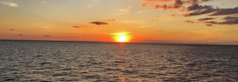 Photo of a sun setting over calm waters and blues skies from the deck of the boat in Cape May New Jersey.
