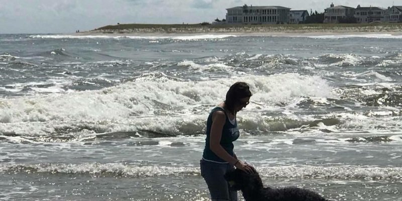 Image of a woman and her dog at Corson's State Park in Ocean City NJ with waves crashing on the beach behind her.