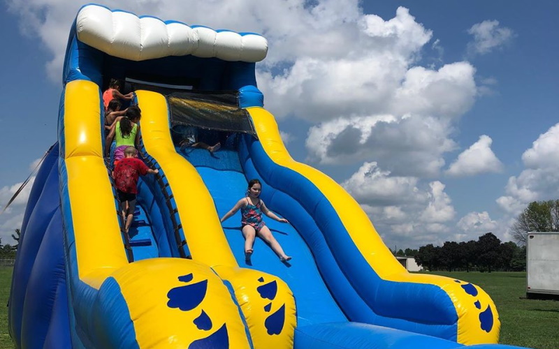 Photo of a little girl sliding down a large blue and yellow inflatable slide with kids walking up the stairs.