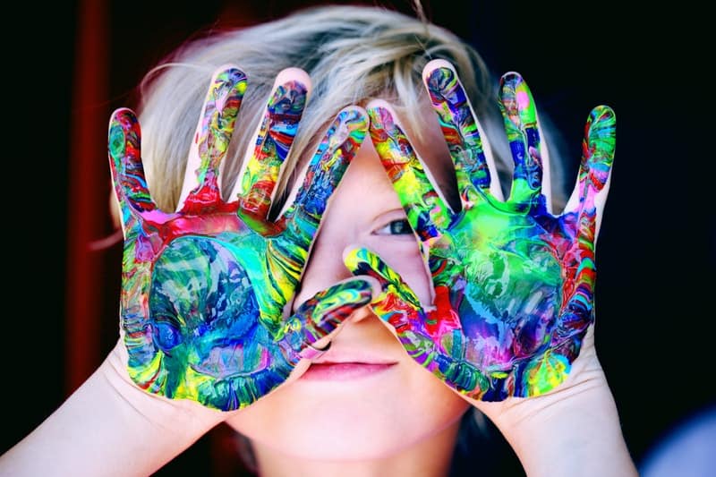 Photo of a kid holding his palms up with a bunch of nicely colored paints completely covering the bottom of his hands. Finger painting is a fun thing to do for kids.