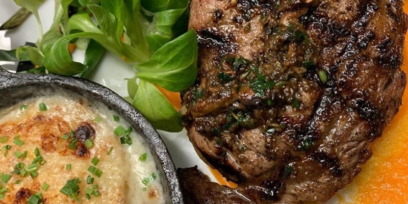 Image a romantic steak and potatoes meal with green basil leaves.=