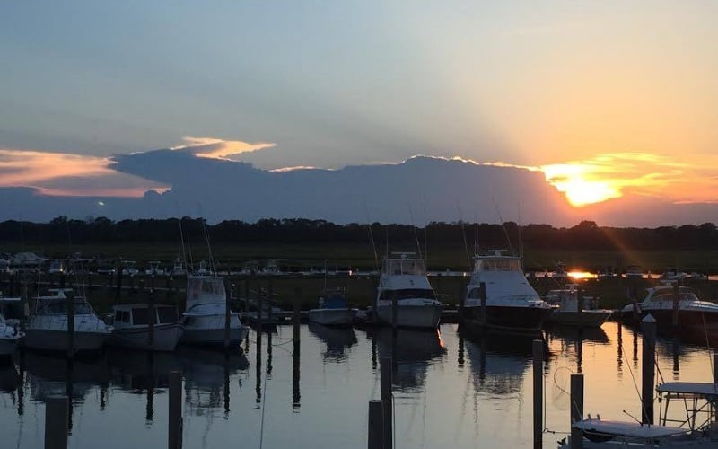 Photo of docks with boats with a sun peaking above clouds.