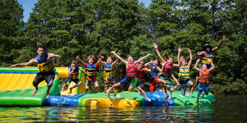 Photo a bunch of children jumping into a lake off a mid lake platform all wearing life vests.