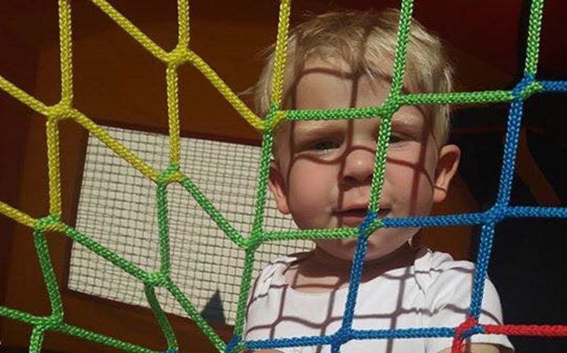 Photo of a blond boylooking through a yellow blue and green safety net on a inflatable bounce house. Finger painting is a fun thing to do for kids.