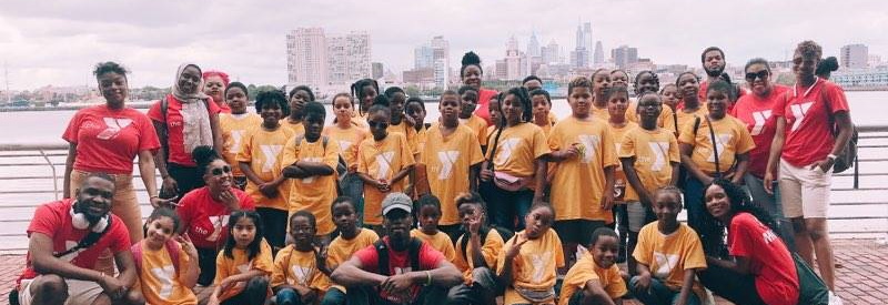 a group of workers and campers standing in front of the NYC skyline dressed in Newarl YMCA camp shirts.