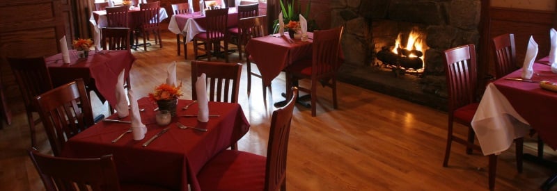 Photo of the dining area of Northwood Inn with a fireplace and red table cloths