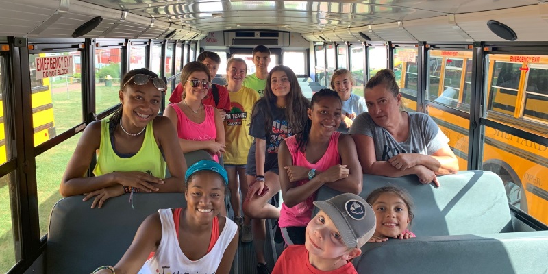 Image children on a yellow school bus smiling for the camera at Oak Crest Day Camp in Somerset NJ.