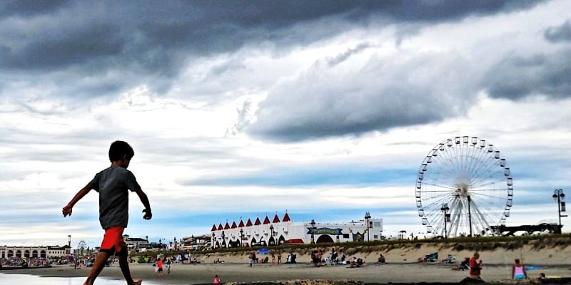 Stylized photo of a little boy walking on the beach with the Ocean City, NJ boardwalk in the background.