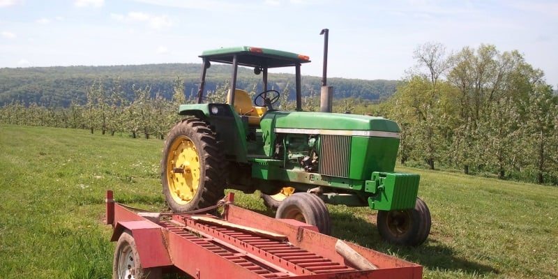 Photo a green tractor sitting on a farm with large rolling hills in the distance and blue sky in Milford, NJ.