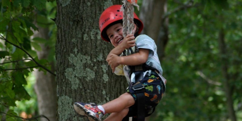 Photo a little boy swinging from a tree in a harness with a red helmet on at a day camp in New Jersey.