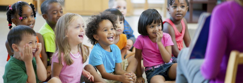 Picture of smiling children getting read a book at a camp in NJ.