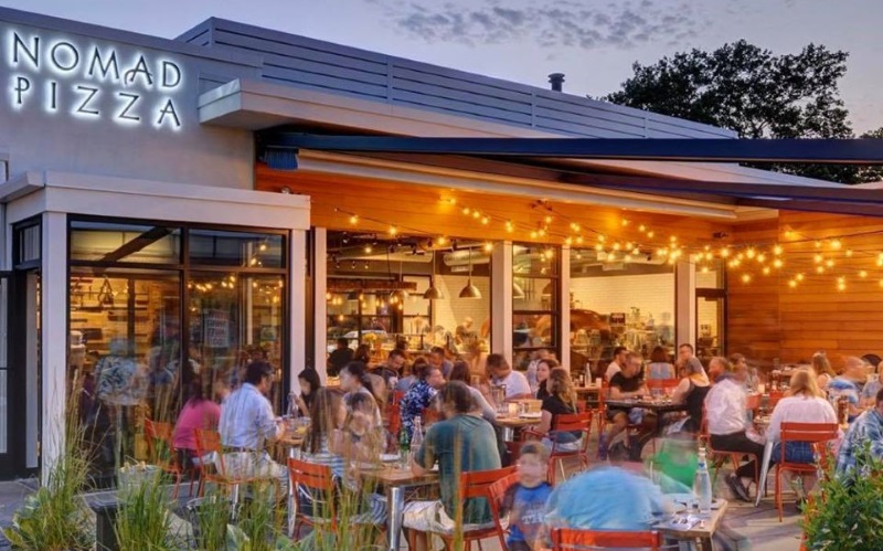 Photo of a people eating outside Nomad Pizza at the princeton shopping center as with hanging yellow lights