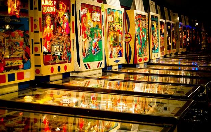 Image of a row of brightly lit up classic and vintage pinball machines.