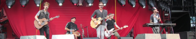 Image of a 5 man band playing a concert at the Lincoln Financial Field in Philadelphia PA. There are three guitar players, a keyboardist and a drummer