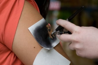 Image of an artist airbrushing a tattoo onto a persons arm as an example of a child's birthday party idea in NJ