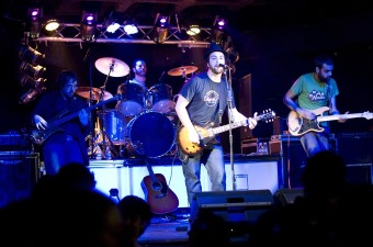 Image of a man on stage with a band singing and playing the guitar as part of the NJ music scene