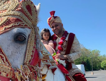 An Indian man and a littlr girl in colorful outfits on a Baraat Horse