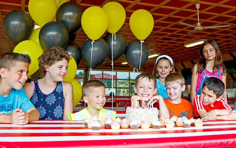 Children sing happy birthday during a Diggerland USA party while child gets ready to blow out the candles.