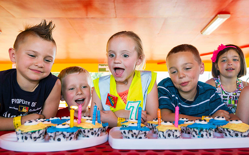 Children sing happy birthday during a Diggerland USA party while child gets ready to blow out the candles.