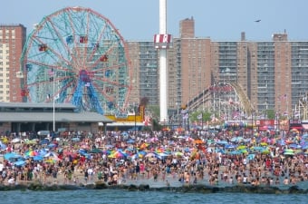 Photo of people on the Coney Island NY boardwalk with a ferris wheel and roller coaster in the background showing fun that goes beyond NJ