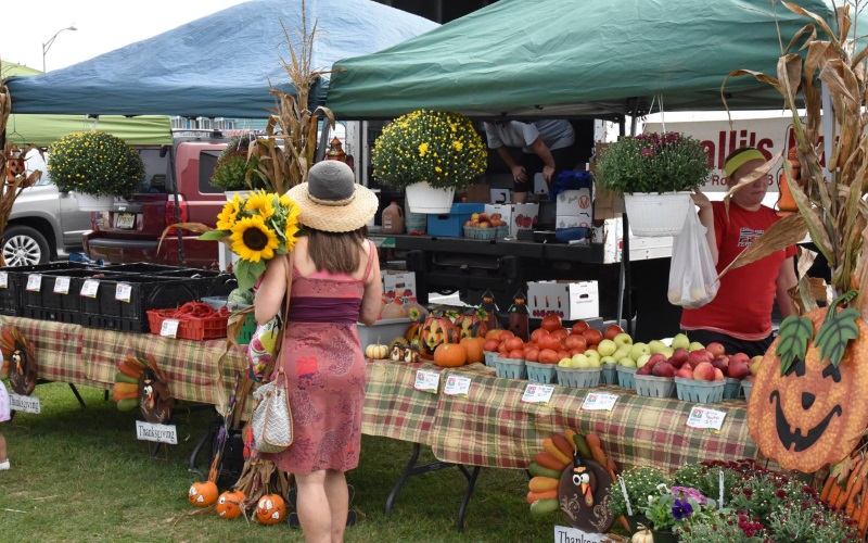 A produce stand with a woman carrying sunflowers