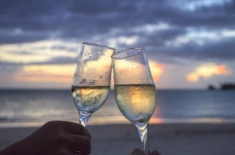 Image of a romantic wedding toast with two champagne glasses half full with a beach (ocean shoreline) behind them at dusk 