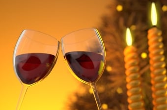 2 wine glasses half full of red wine clinking next to 2 candles with an orange backround