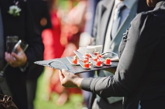 A person in a gray jacket holding a tray of orange colored hors d'oeuvres