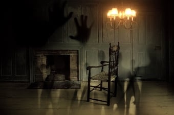 A spooky dimly lit image of a rocking chair with a chandelier above the chair