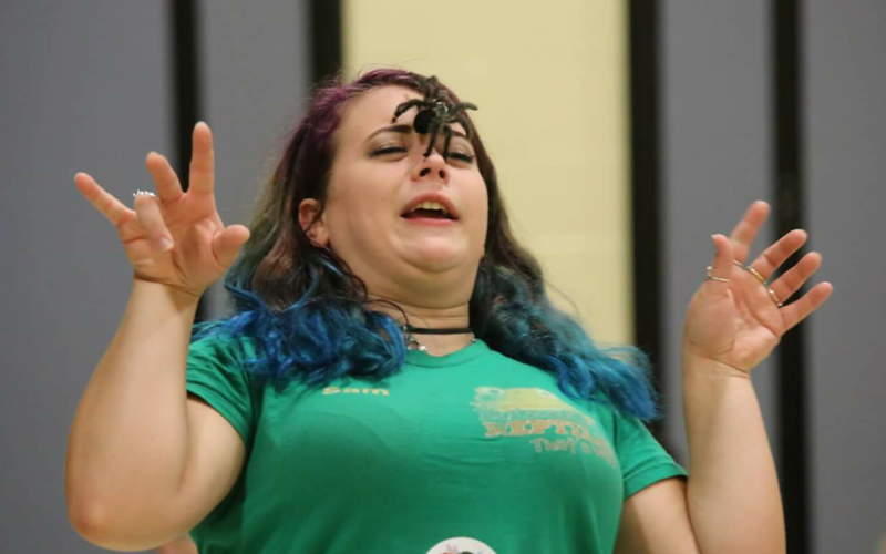 Photo of a girl with a green shirt colorful hair and a spider on her face.
